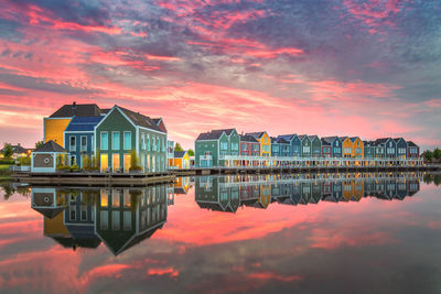 Reflection of buildings on lake against sky during sunset
