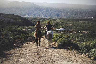 People riding horses on mountain road against sky