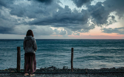 Rear view of young woman standing by sea against sky