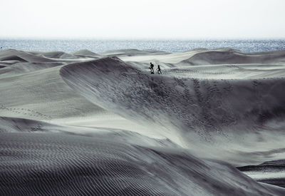 Distant view of couple walking at desert against sea