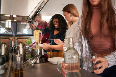 Content young multiethnic female friends in casual wear putting tasty spaghetti on plate near counter in modern self service restaurant