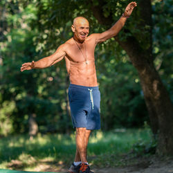 Full length of shirtless man standing against trees