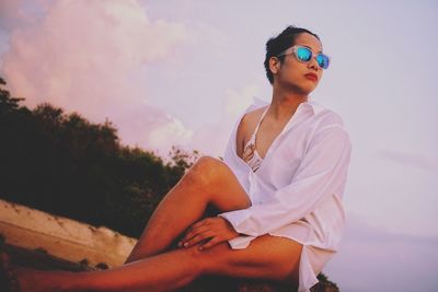 Low angle view of seductive woman sitting at beach against sky during sunset