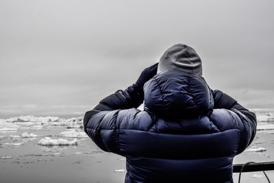 Rear view of man wearing warm clothing while standing against sea during winter