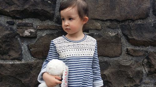 Cute girl with stuffed toy standing against stone wall