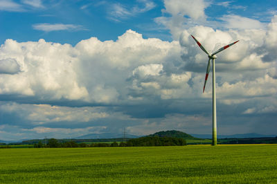 Single wind turbine on a green field in front of dramatic sky