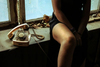 Midsection of woman by rotary phone on window sill