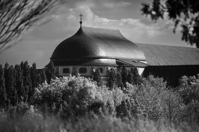 Roof of a church behind a high meadow and bushes in black and white.