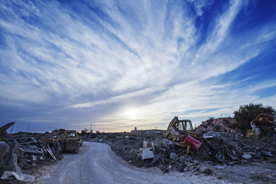 Road amidst junkyard against sky during sunset