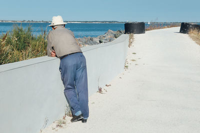 Rear view of man leaning on railing against sea