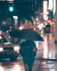 Rear view of man walking with umbrella in rainy season