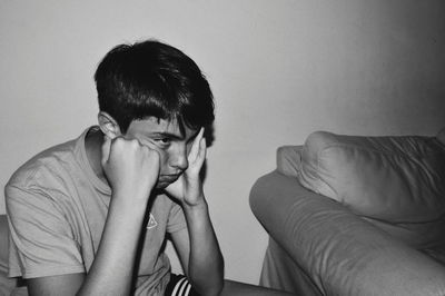 Portrait of young man sitting against wall at home