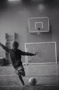 Rear view of boy kicking ball at court