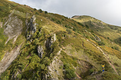 Rear view of young woman in yellow hoodie with backpack hiking in picturesque mountain valley