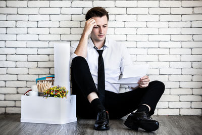 Young man using mobile phone while sitting on wall