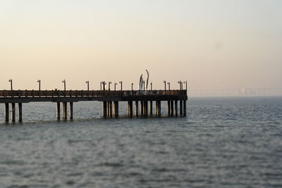 Pier over sea against clear sky during sunset
