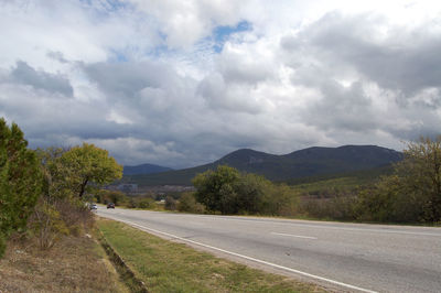 Empty road by trees against sky