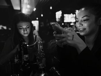 Smiling friends using phones by bottles on table in nightclub
