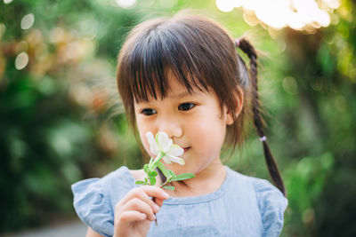 Close-up of cute girl holding flower while standing outdoors