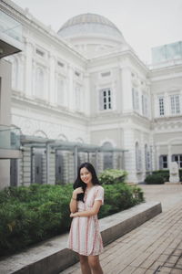 Portrait of smiling young woman standing against building