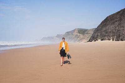 Rear view of man walking on beach against clear sky