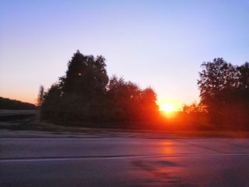 Silhouette trees by road against sky during sunset