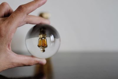 Upside down image of perfume bottle reflecting in crystal ball held by hand