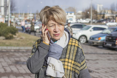 A cute older woman in casual clothes is talking on the phone on a city street in the spring. 