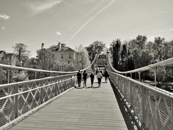 People walking on bridge amidst trees against sky