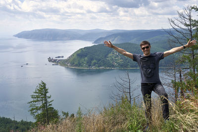 Young man with arms raised on mountain against sky