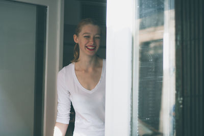 Cheerful woman standing by windows on sunny day