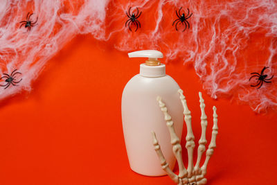 Cosmetic bottle with oil or soap on red halloween background with spiders and skeleton hands