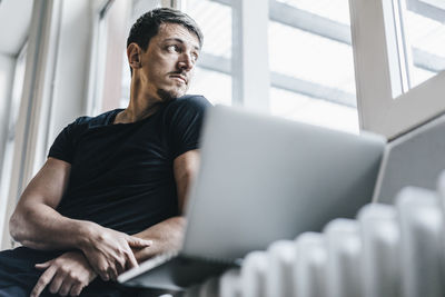 Man sitting on heater with laptop