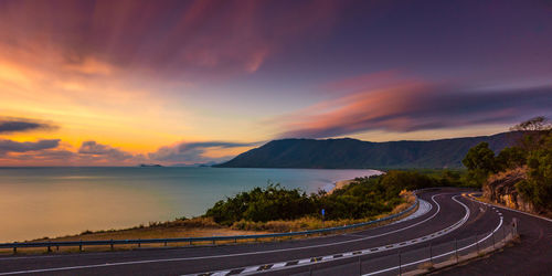 Road by sea against sky during sunset