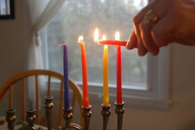 Cropped image of woman igniting candles on hanukkah at home