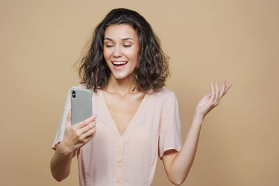 Portrait of young woman using mobile phone against wall
