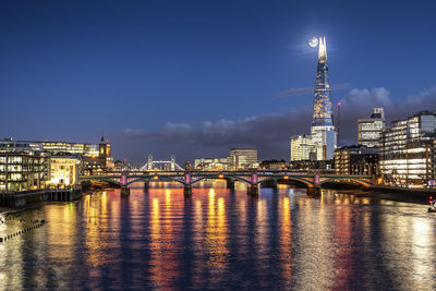 Illuminated bridge over river against buildings at night