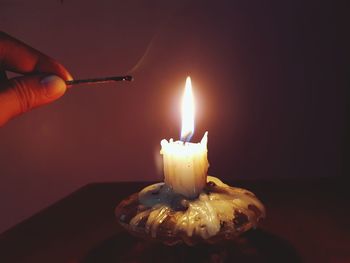 Cropped hand holding burnt matchstick by lit candle on table in darkroom