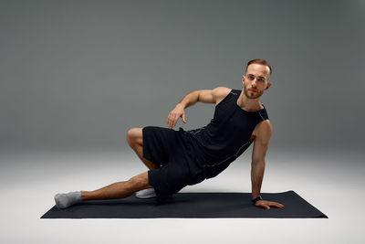 Side view of woman exercising against black background