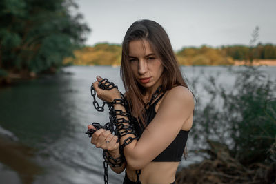 Portrait of young woman standing against lake during sunset