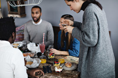 Young woman photographing food on dining table amidst friends at restaurant