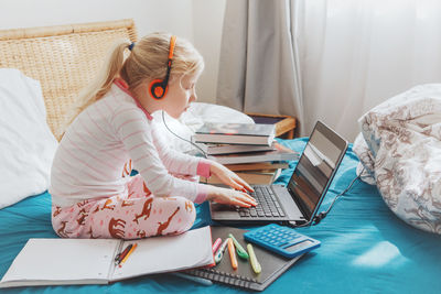 Cute girl using laptop sitting on bed at home