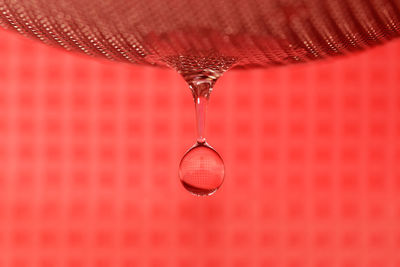 Close-up of falling water drop over red background