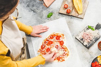 Caucasian teenage girl in an apron pouring grated cheese on pizza hearts .