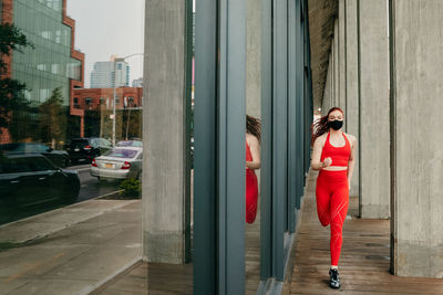 Young woman in red sportswear, running in street, wearing a face mask.