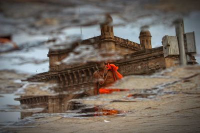 Reflection of monk and building in puddle on footpath