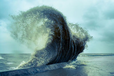 Sea waves splashing on shore against sky