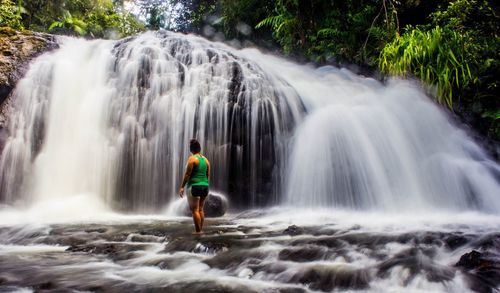 Rear view of woman standing by waterfall