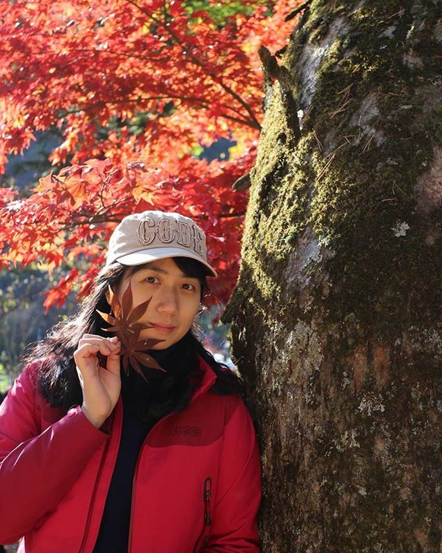 lifestyles, leisure activity, casual clothing, tree, looking at camera, person, young adult, red, standing, portrait, front view, smiling, warm clothing, young women, tree trunk, three quarter length, forest, day