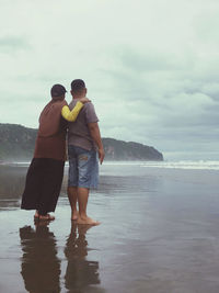 Rear view of man standing at beach against sky